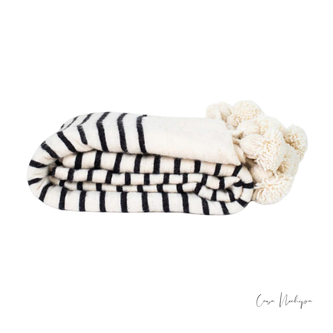 Frazada artesanal blanca con negro y borlas decorativas, tejida en telar de pedal