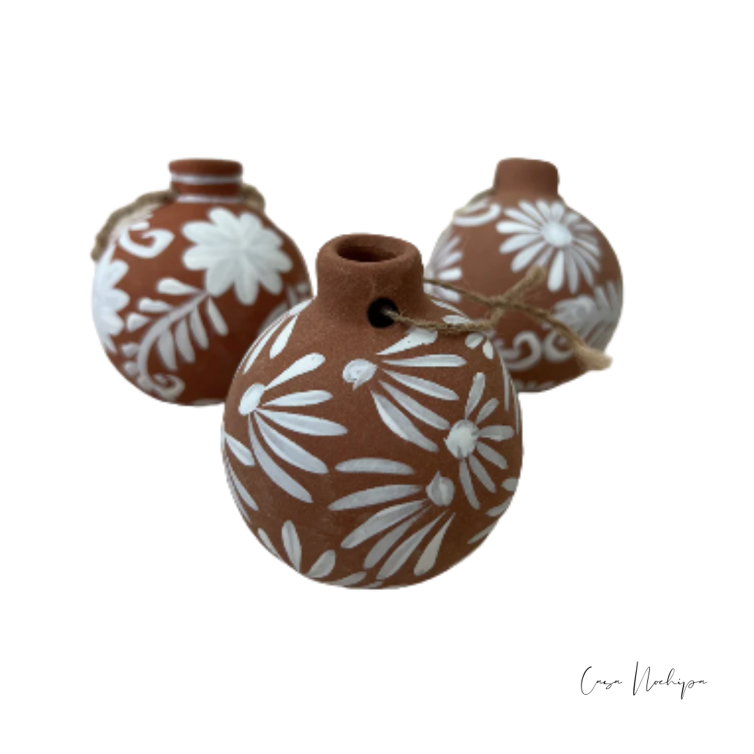 Esferas de barro terracota pintadas a mano con flores blancas, ornamentación navideña artesanal.