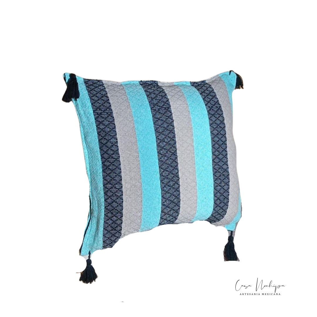 Cojín artesanal en tonos azul y gris, tejido en telar de pedal con borlas decorativas. Algodón orgánico, diseño tradicional de Oaxaca.