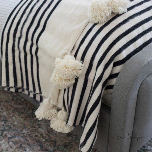 Frazada artesanal blanca con negro y borlas decorativas, tejida en telar de pedal