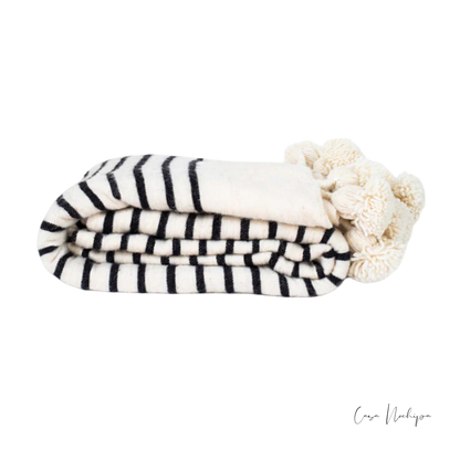 Frazada artesanal blanca con negro y borlas decorativas, tejida en telar de pedal