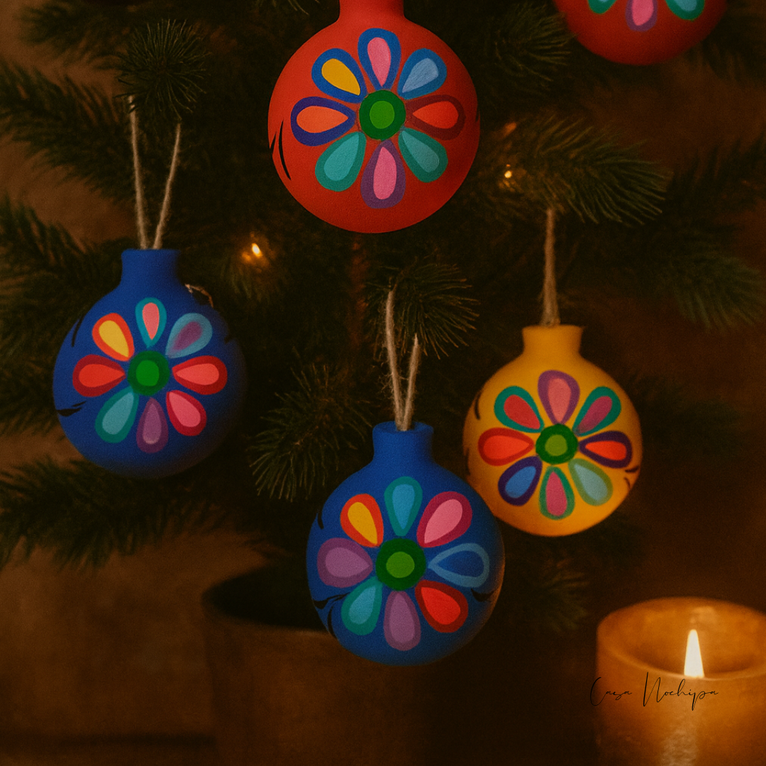Esfera navideña morada de barro con diseño floral pintado a mano en colores vivos.